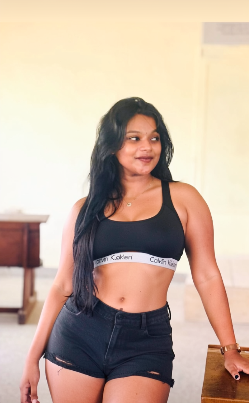 Change her top to a black Calvin Klein sports bra, straight-across neckline, high coverage, modest subtle cleavage, wide branded underband, fitted cropped style, no deep V neck showing navel. And a tight sexy revealing black denim shorts showing navel