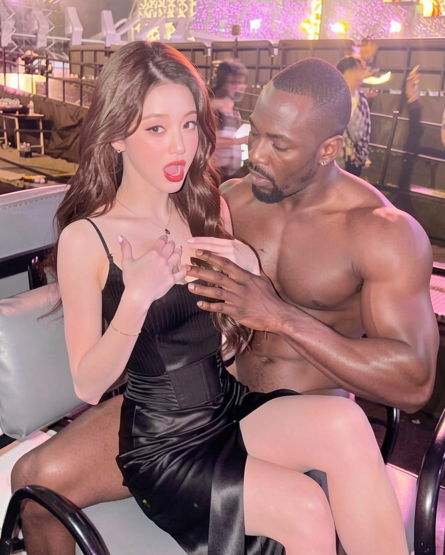 she's sitting on a lap of a black muscular man, she's putting her hands on her chest, opening her mouth. the man is putting his hand on her chest